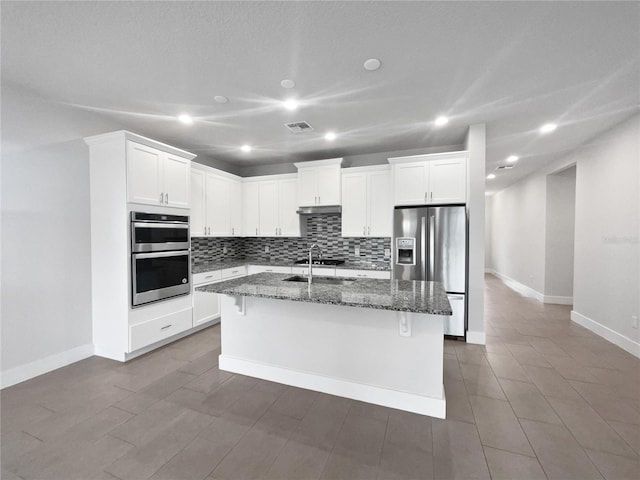 kitchen with a breakfast bar area, white cabinetry, dark stone countertops, stainless steel appliances, and a center island with sink