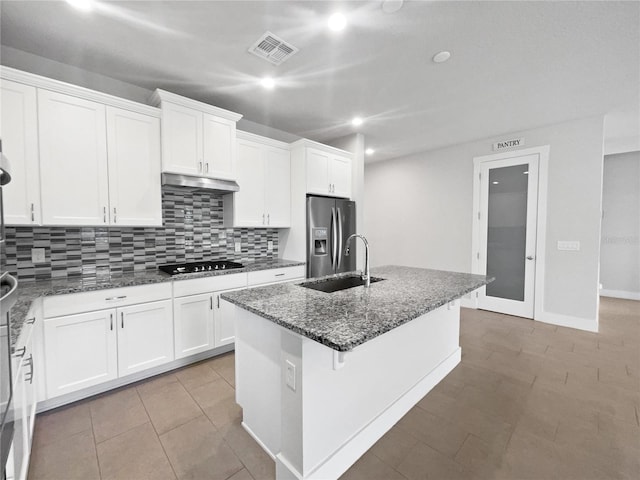 kitchen with sink, stainless steel fridge, an island with sink, and dark stone countertops