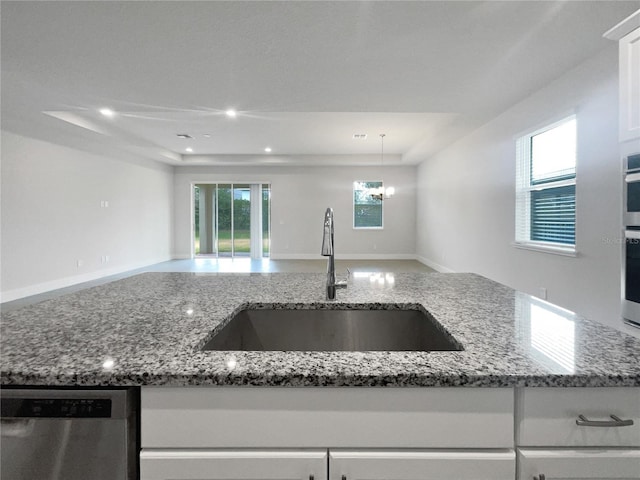 kitchen with sink, dishwasher, stone counters, white cabinetry, and a tray ceiling