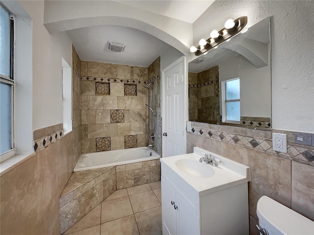 full bathroom featuring tile walls, tiled shower / bath combo, vanity, toilet, and tile patterned floors