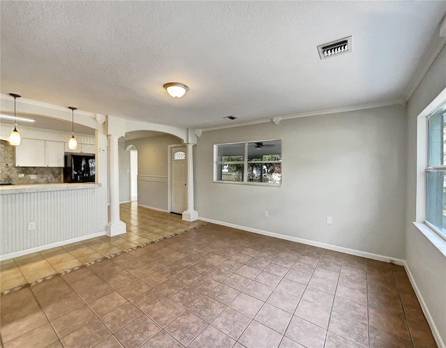 unfurnished living room featuring crown molding, light tile patterned floors, a textured ceiling, and ornate columns