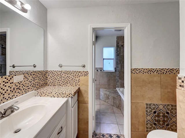 bathroom featuring tile walls, tiled tub, vanity, and tile patterned flooring