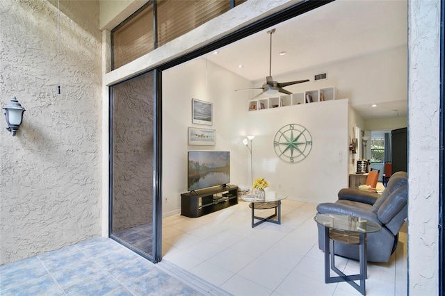 living room featuring ceiling fan, light tile patterned flooring, and a high ceiling