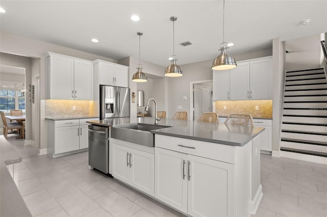 kitchen featuring sink, appliances with stainless steel finishes, a kitchen island with sink, white cabinetry, and decorative light fixtures