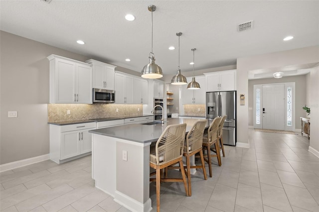 kitchen with sink, white cabinetry, decorative light fixtures, appliances with stainless steel finishes, and an island with sink