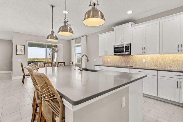 kitchen featuring sink, white cabinetry, an island with sink, pendant lighting, and decorative backsplash