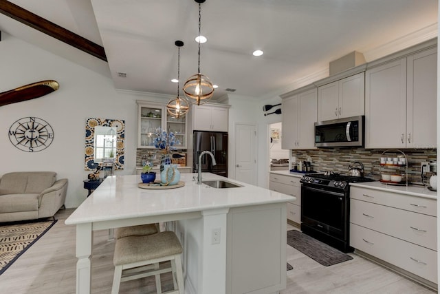 kitchen with a kitchen island with sink, sink, pendant lighting, and black appliances