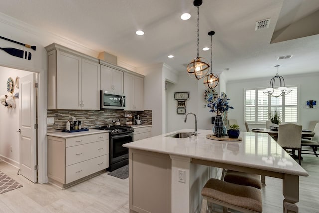 kitchen featuring sink, range with gas cooktop, crown molding, hanging light fixtures, and a center island with sink