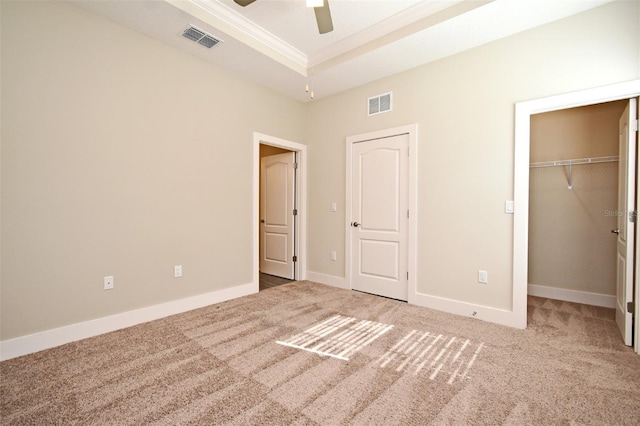 unfurnished bedroom featuring carpet, ornamental molding, a raised ceiling, a walk in closet, and a closet