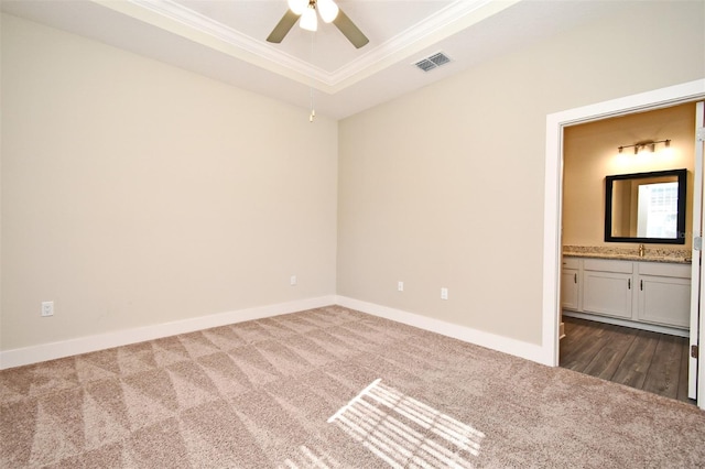 unfurnished bedroom featuring connected bathroom, sink, ornamental molding, a raised ceiling, and dark carpet