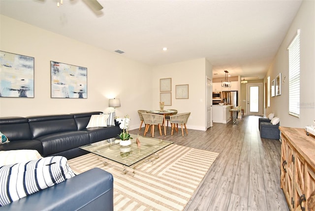 living room with baseboards, ceiling fan, visible vents, and light wood-style floors