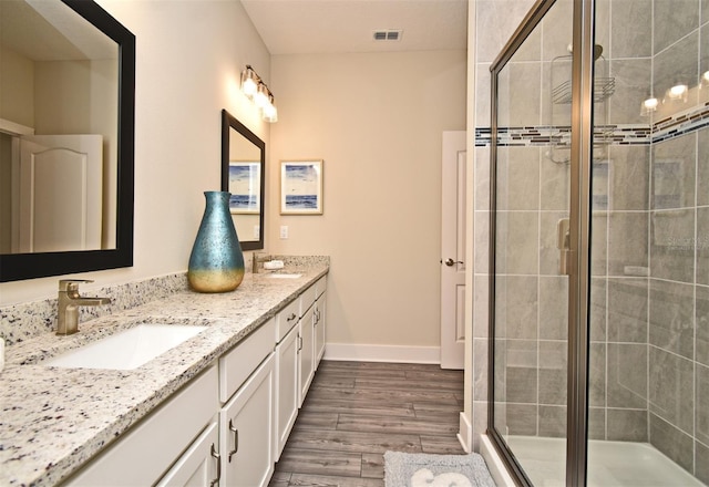 bathroom featuring a shower stall, a sink, visible vents, double vanity, and wood finished floors