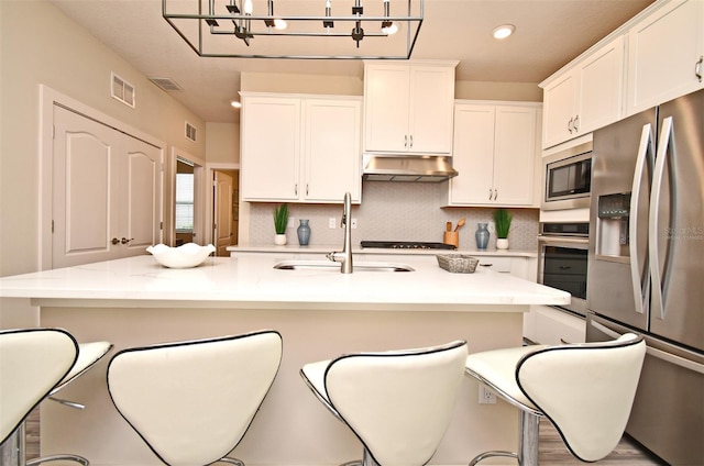 kitchen with a sink, tasteful backsplash, under cabinet range hood, stainless steel appliances, and visible vents