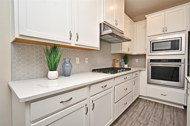 kitchen with light countertops, stainless steel appliances, under cabinet range hood, white cabinetry, and backsplash