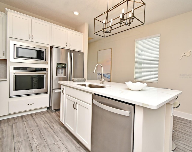 kitchen featuring a sink, white cabinetry, appliances with stainless steel finishes, light wood-style flooring, and an inviting chandelier