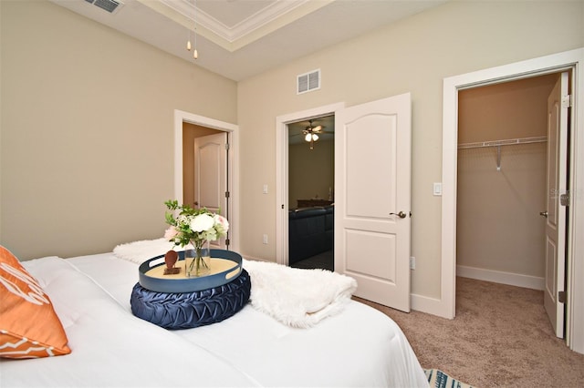 bedroom featuring a closet, visible vents, carpet, a tray ceiling, and a walk in closet