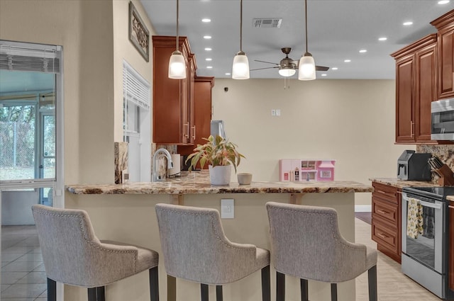 kitchen featuring light stone counters, stainless steel appliances, decorative light fixtures, and a breakfast bar area