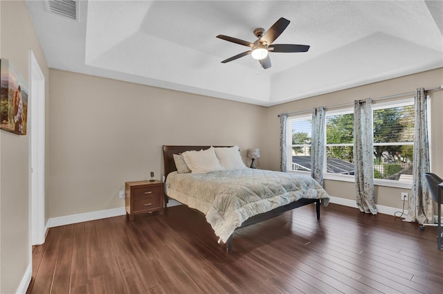 bedroom with a tray ceiling, dark hardwood / wood-style floors, and ceiling fan