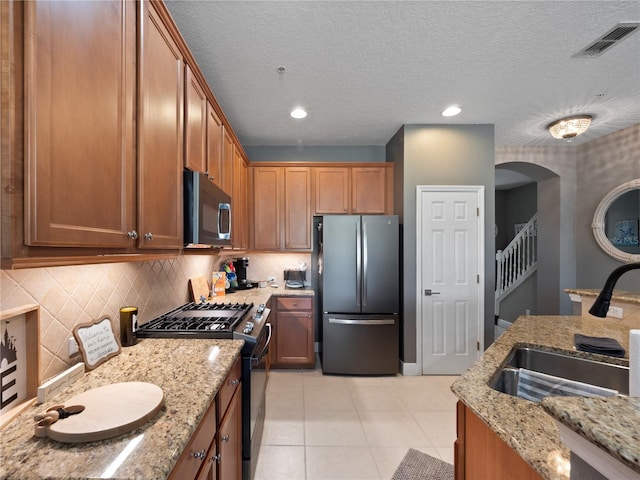 kitchen with sink, light tile patterned floors, appliances with stainless steel finishes, light stone countertops, and backsplash