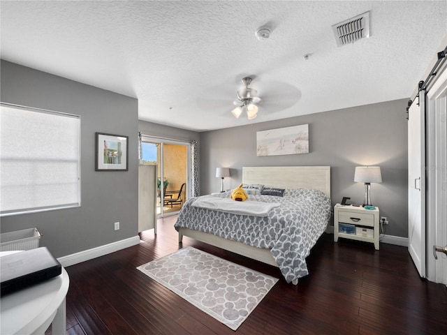 bedroom featuring ceiling fan, dark wood-type flooring, a barn door, and a textured ceiling