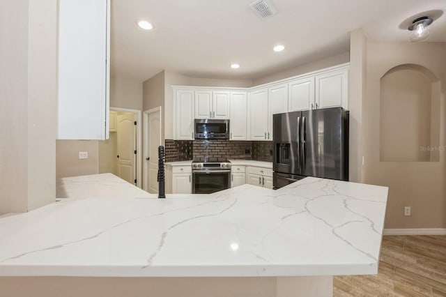 kitchen with white cabinetry, appliances with stainless steel finishes, kitchen peninsula, and light stone counters