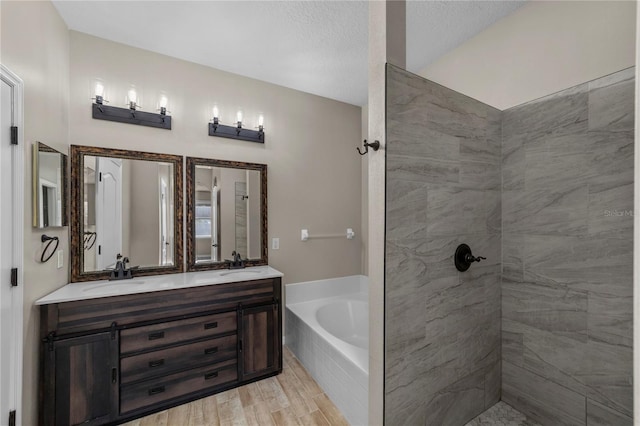 bathroom with a relaxing tiled tub, vanity, hardwood / wood-style floors, and a textured ceiling