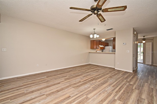 unfurnished living room featuring wood-type flooring, ceiling fan with notable chandelier, and a textured ceiling