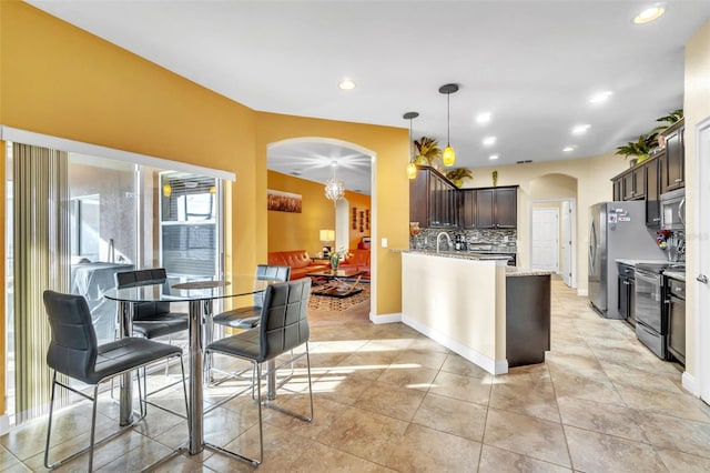 kitchen featuring pendant lighting, appliances with stainless steel finishes, backsplash, dark brown cabinetry, and light stone countertops