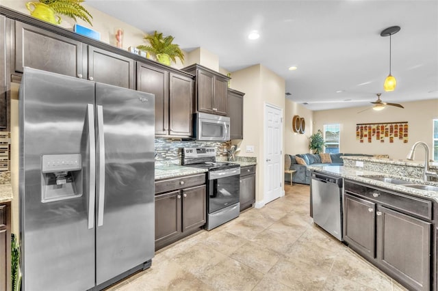 kitchen featuring sink, appliances with stainless steel finishes, dark brown cabinets, light stone counters, and decorative light fixtures