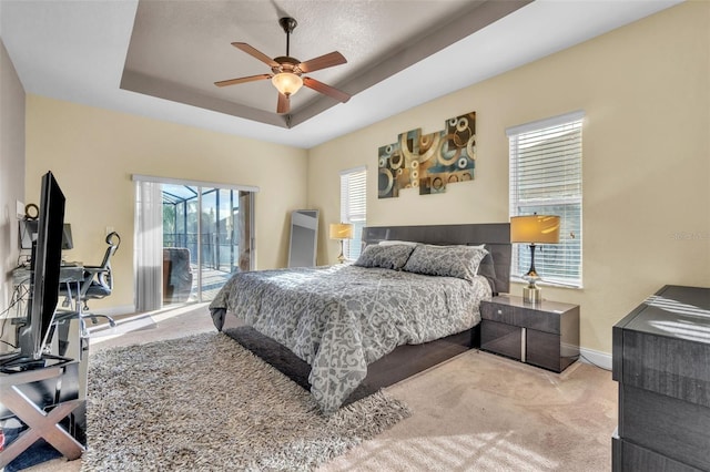 bedroom featuring access to exterior, a tray ceiling, light colored carpet, and ceiling fan