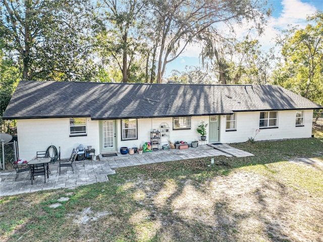 back of property with a patio area, concrete block siding, a lawn, and roof with shingles