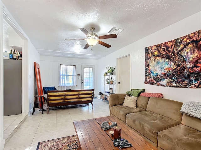 living area featuring light tile patterned floors, a ceiling fan, visible vents, and a textured ceiling