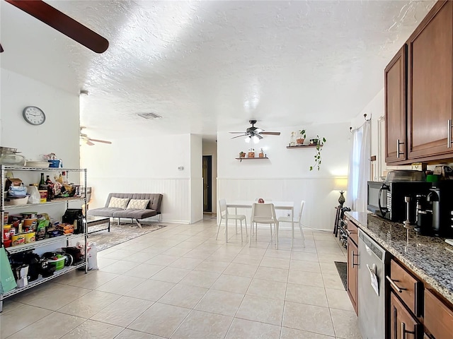 kitchen with a wainscoted wall, ceiling fan, a textured ceiling, stainless steel dishwasher, and light tile patterned flooring