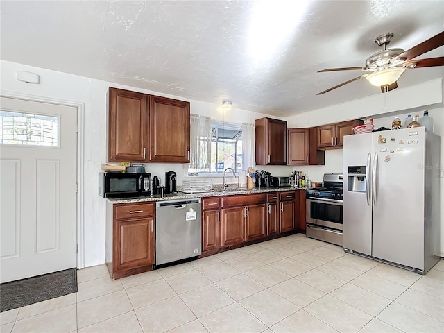 kitchen with stone counters, light tile patterned floors, appliances with stainless steel finishes, a sink, and ceiling fan