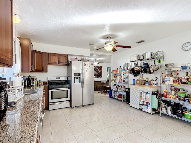 kitchen featuring light tile patterned floors, a textured ceiling, a sink, appliances with stainless steel finishes, and light stone countertops