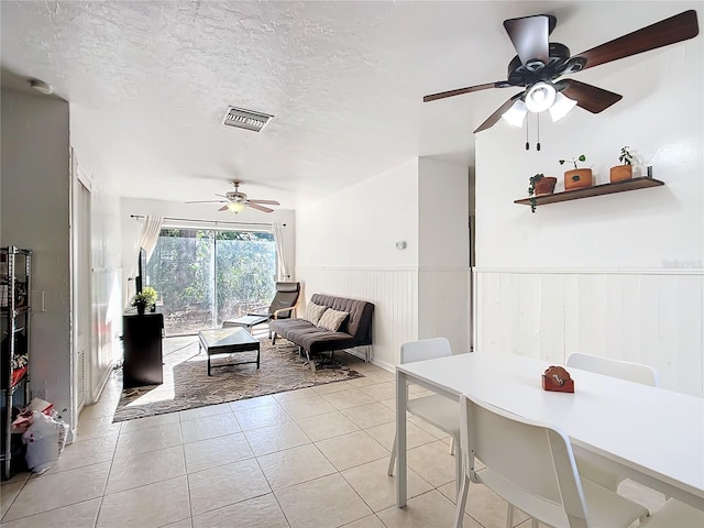 interior space featuring light tile patterned floors, visible vents, a ceiling fan, wainscoting, and a textured ceiling