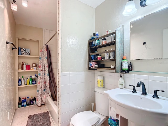 full bath with tile walls, a textured wall, toilet, a sink, and tile patterned flooring