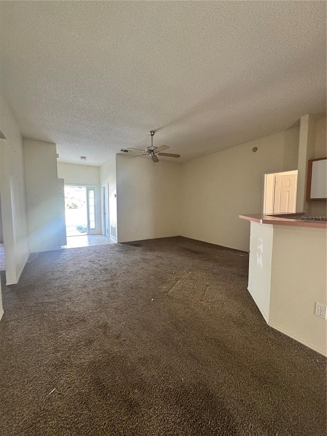 unfurnished living room with ceiling fan, a textured ceiling, and dark colored carpet