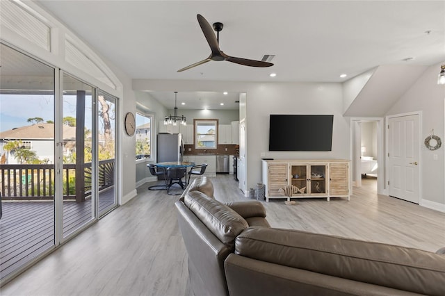 living room featuring ceiling fan with notable chandelier and light wood-type flooring