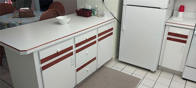 kitchen with light tile patterned floors, kitchen peninsula, white cabinets, and white refrigerator