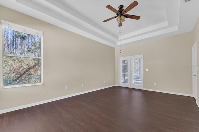 empty room with dark hardwood / wood-style flooring, a raised ceiling, ceiling fan, and french doors