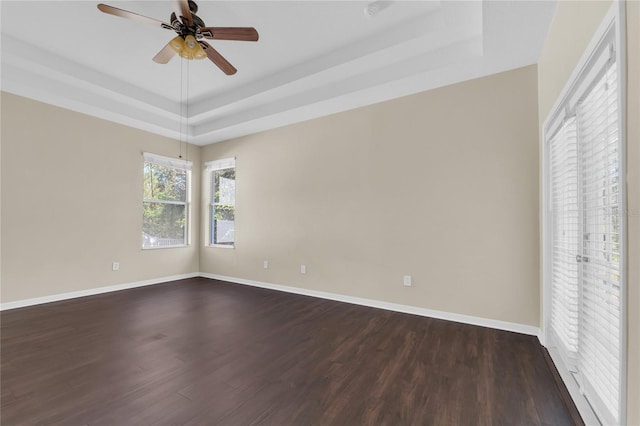 unfurnished room with ceiling fan, a tray ceiling, and dark hardwood / wood-style flooring