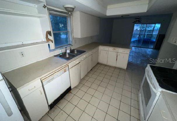 kitchen featuring sink, white appliances, light tile patterned floors, white cabinetry, and a raised ceiling