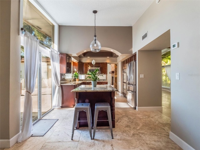 kitchen with stainless steel fridge, hanging light fixtures, a center island, light stone counters, and a kitchen bar