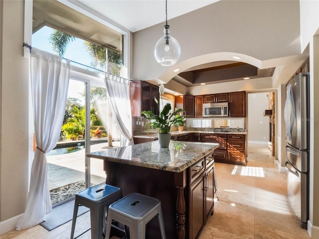 kitchen featuring appliances with stainless steel finishes, dark stone countertops, a kitchen bar, hanging light fixtures, and a center island