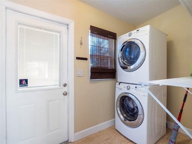 laundry room featuring stacked washer and dryer, light tile patterned floors, and a textured ceiling