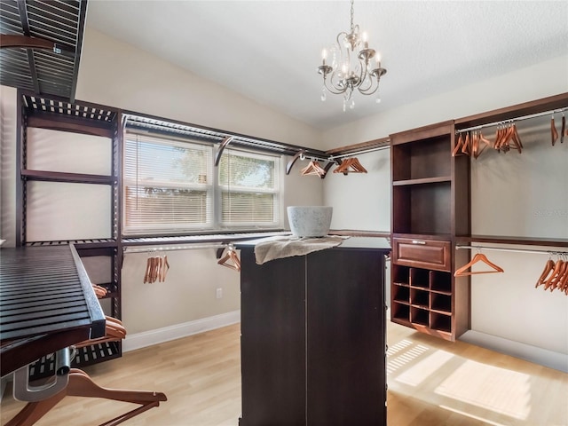 walk in closet featuring a notable chandelier, light hardwood / wood-style flooring, and vaulted ceiling