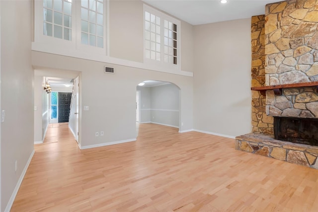 unfurnished living room featuring light wood-type flooring, a fireplace, and a towering ceiling