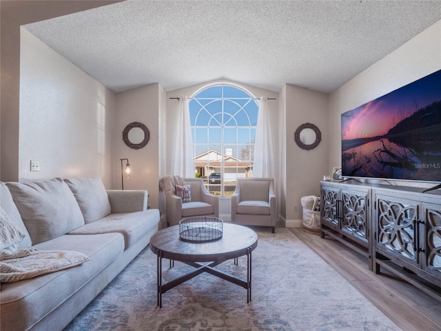 living room with light hardwood / wood-style flooring, a textured ceiling, and vaulted ceiling