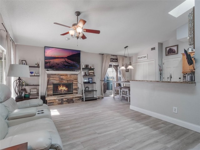 living room featuring ceiling fan, lofted ceiling with skylight, a fireplace, and light wood-type flooring